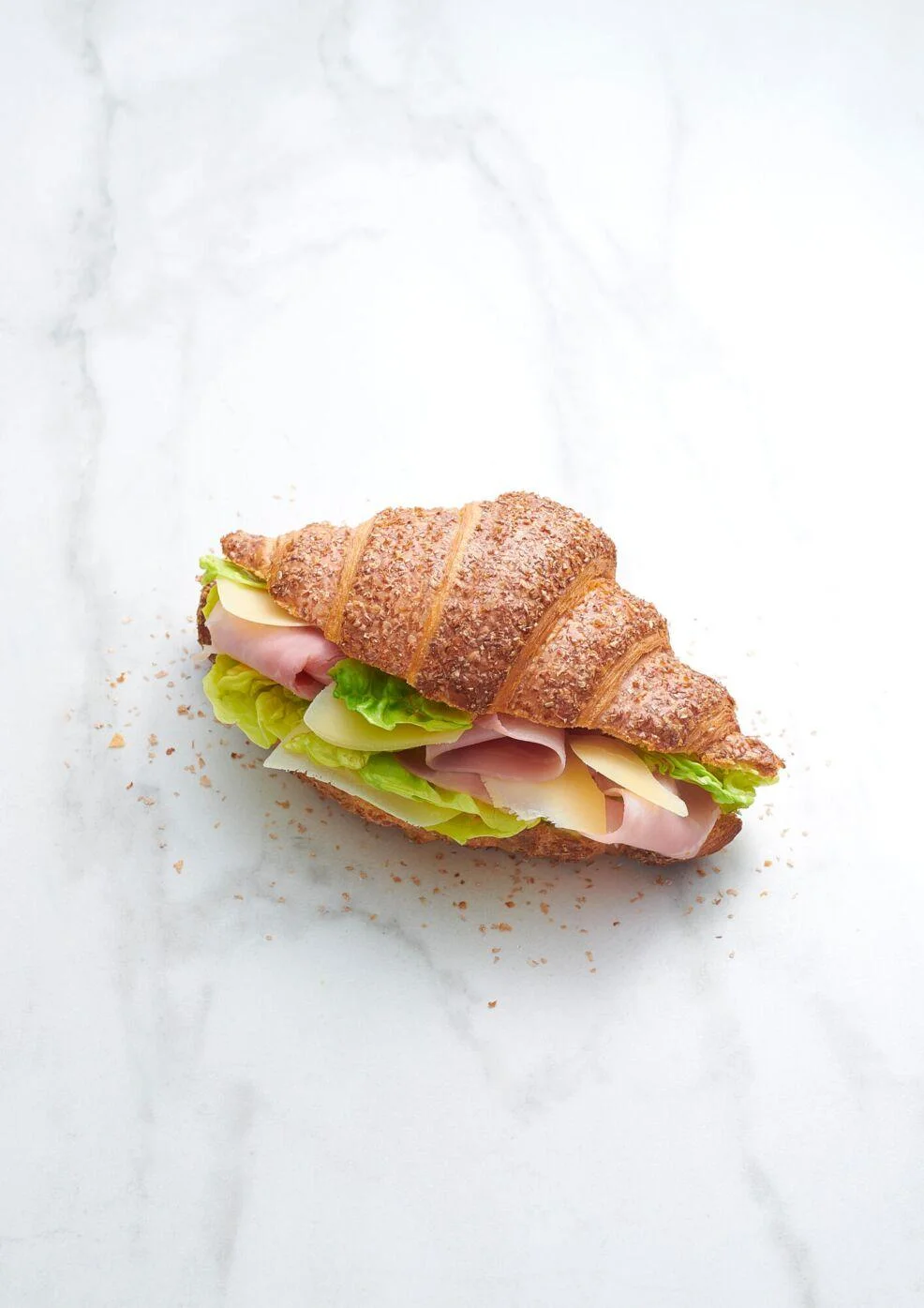 Croissant sandwich with ham, Swiss cheese, lettuce and tomato on a light marble surface
